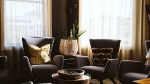 A modern living room with dark furniture, a large window with sheer curtains, and a hanging light fixture. - The State Hotel (New Plymouth)
