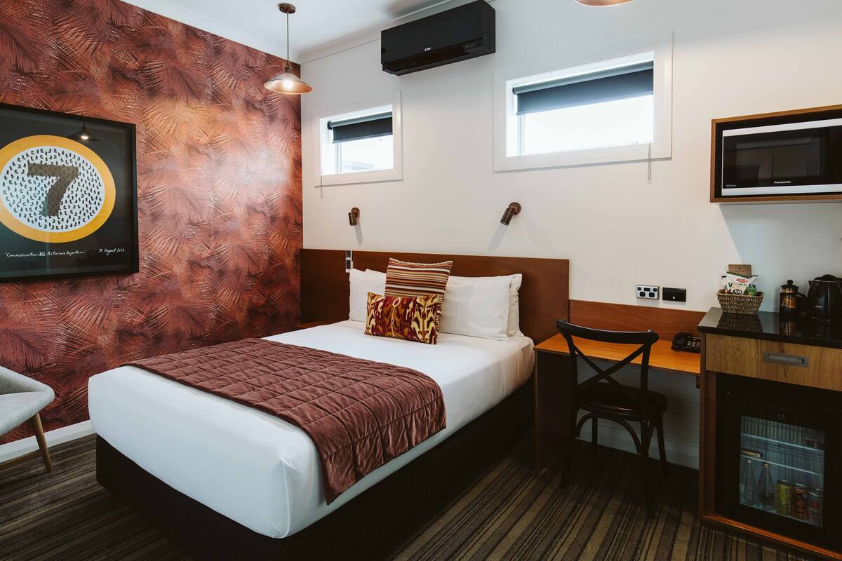 A hotel room with a bed, a desk, a chair, a television, and a wall-mounted air conditioner.