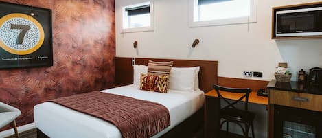 A hotel room with a bed, a desk, a chair, a television, and a wall-mounted air conditioner.