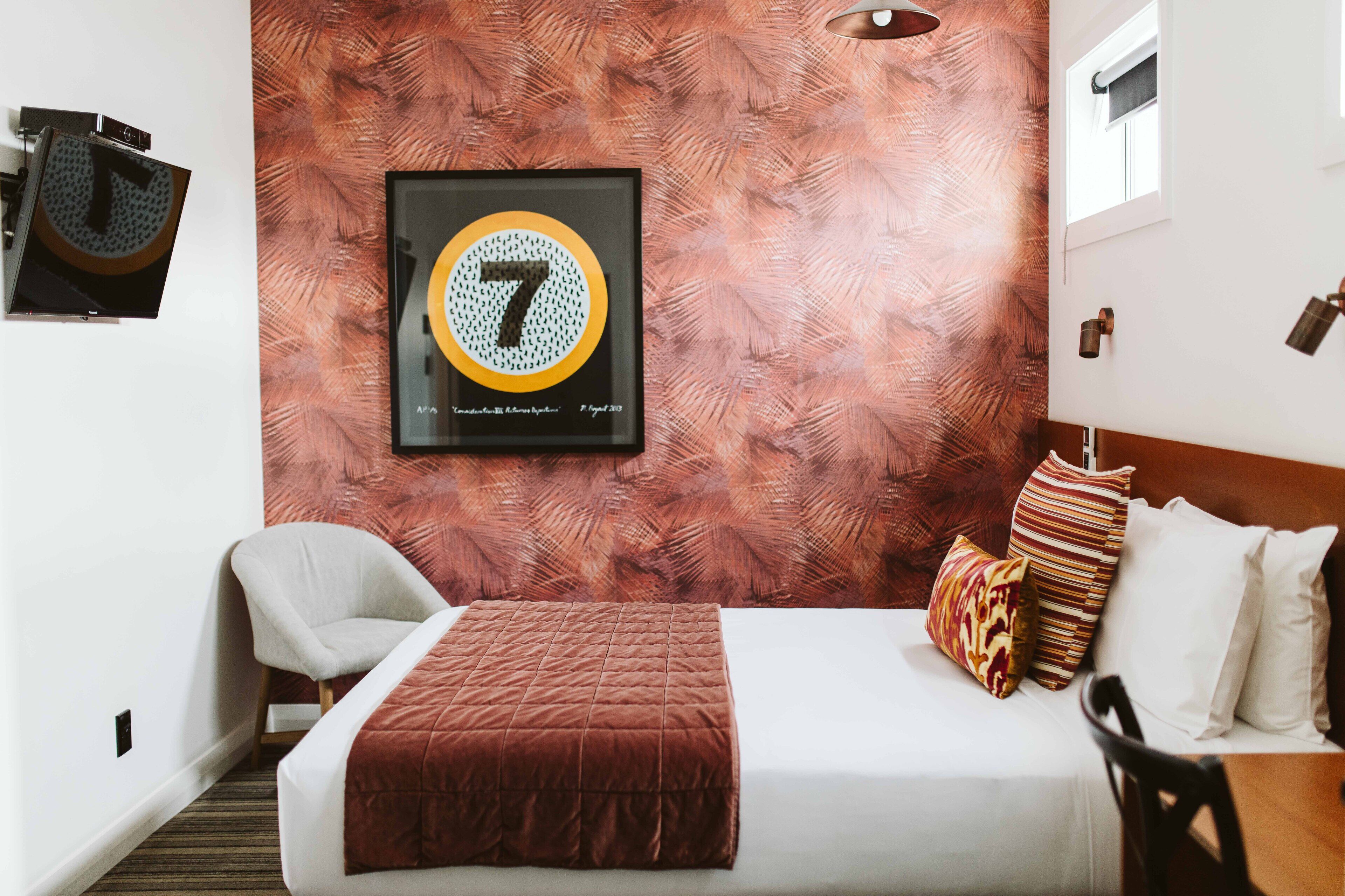 Quarto de hotel com uma cama, uma cadeira, uma obra de arte emoldurada na parede e uma janela.