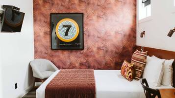 Quarto de hotel com uma cama, uma cadeira, uma obra de arte emoldurada na parede e uma janela.