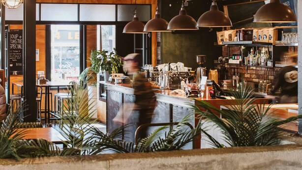 A restaurant with exposed wooden beams, pendant lighting, a bar area, and seating. - The State Hotel (New Plymouth)