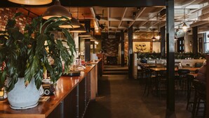 A restaurant interior with exposed brick walls, wooden tables, hanging pendant lights, and a central brick fireplace. - The State Hotel (New Plymouth)