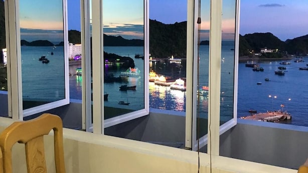 A dining area with a glass table and chairs, overlooking a bay with boats and a dock. - My Ngoc Hotel Catba (Hai Phong)