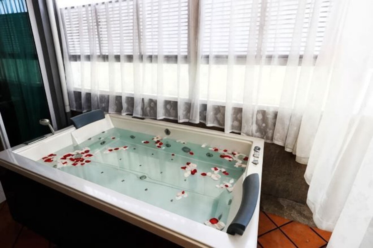 Un espace spa doté d’une baignoire entourée de parois en verre, de rideaux blancs et offrant une vue par la fenêtre.