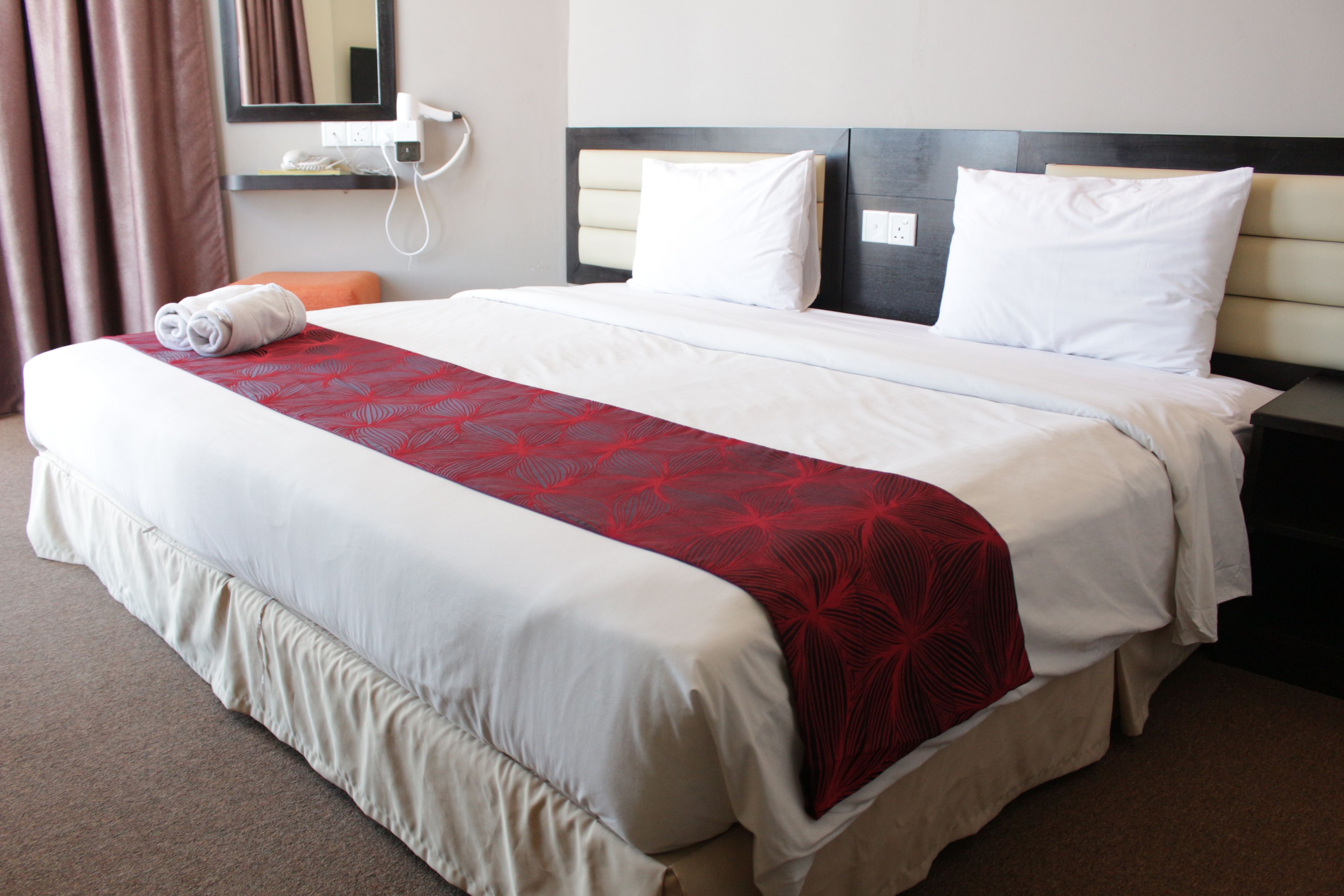 A hotel room with a large bed, a bedside table, a wall-mounted phone, and a window with curtains.