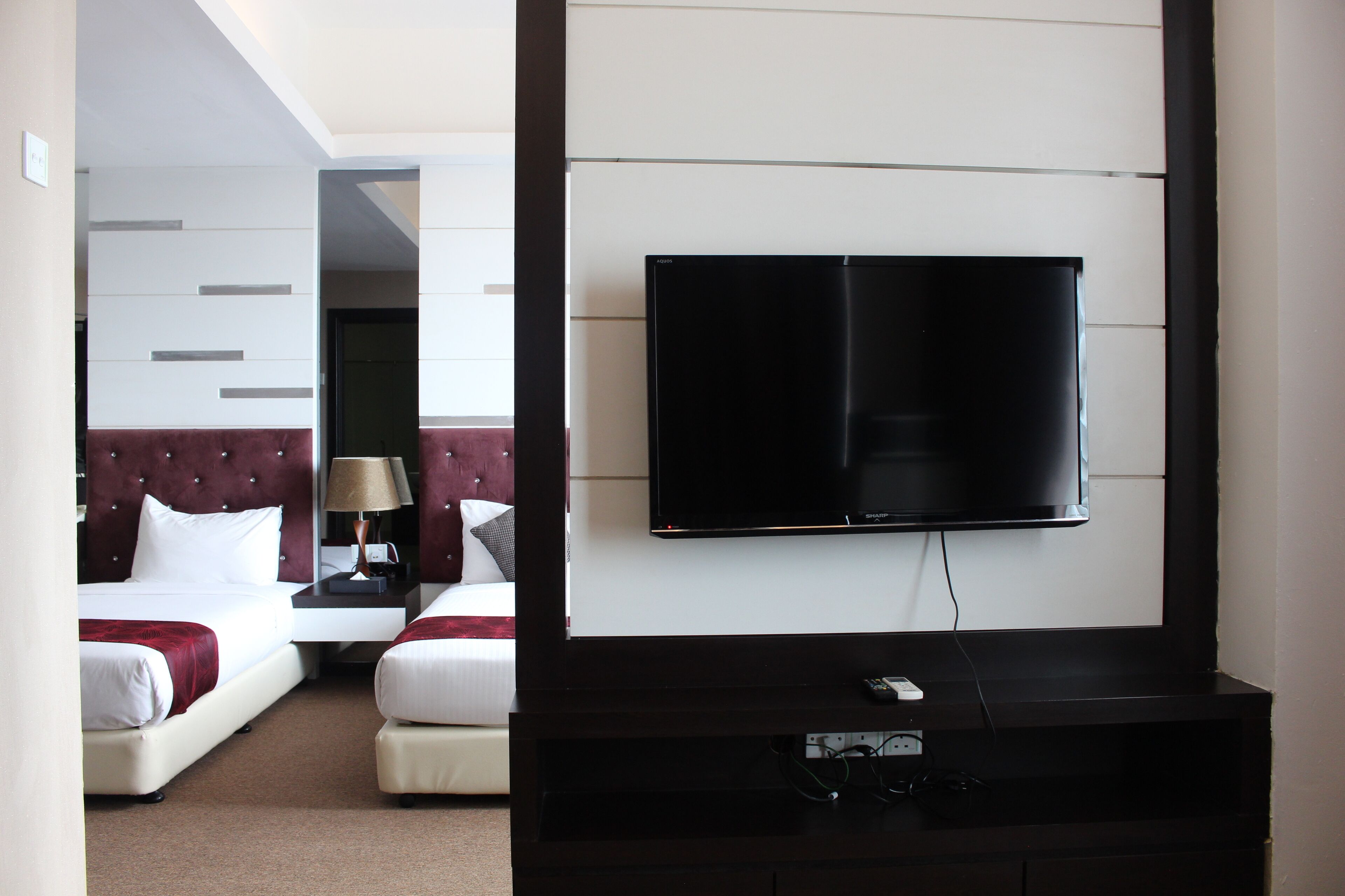 Habitación de hotel con cama, televisión montada en la pared y mesita de noche con lámpara.