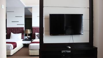 Habitación de hotel con cama, televisión montada en la pared y mesita de noche con lámpara.