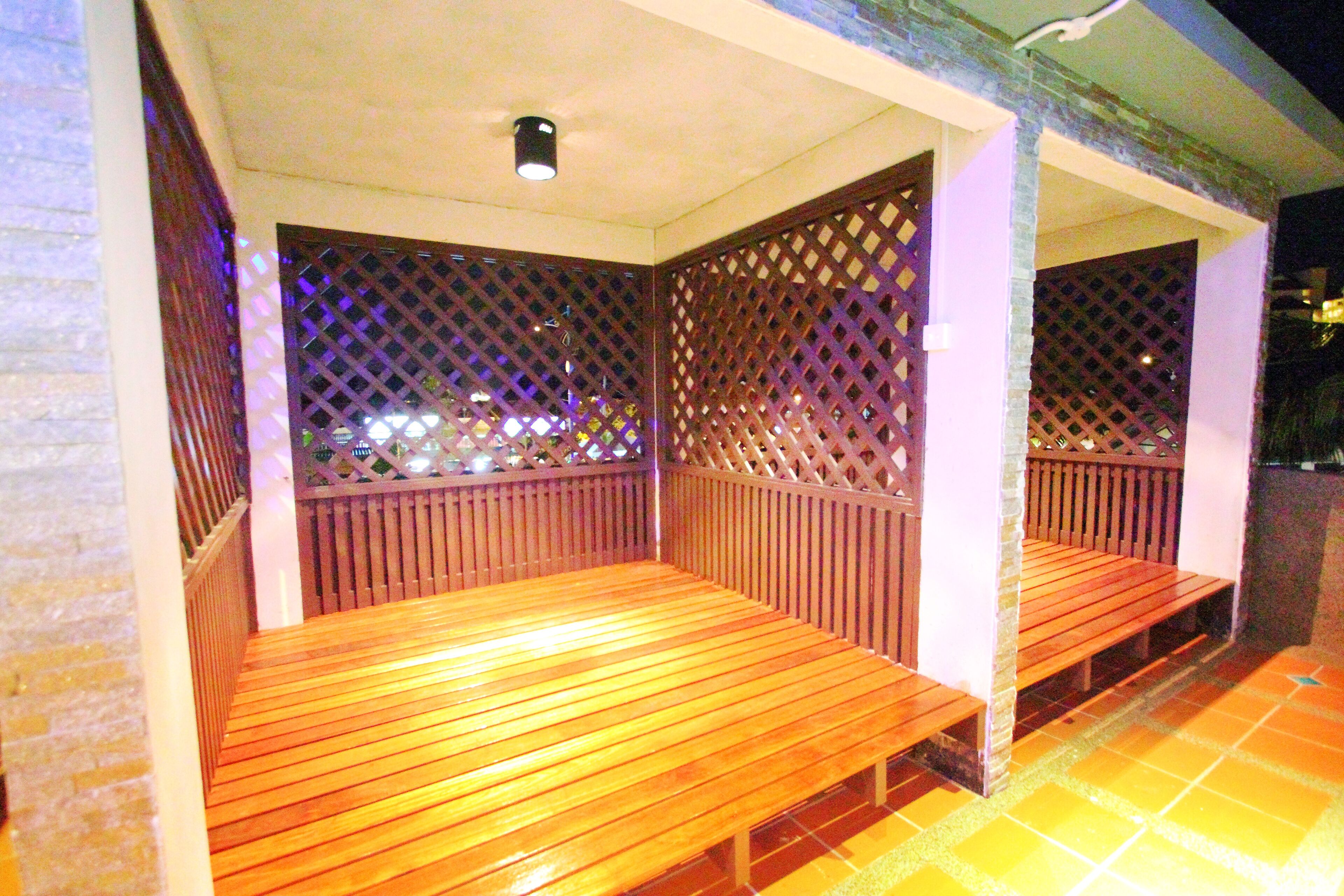 A covered outdoor seating area with wooden benches and lattice partitions.