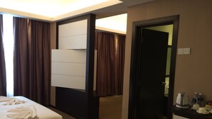 Habitación de hotel con dos camas, un escritorio con tetera y botellas de agua, y una puerta que da a otra habitación.