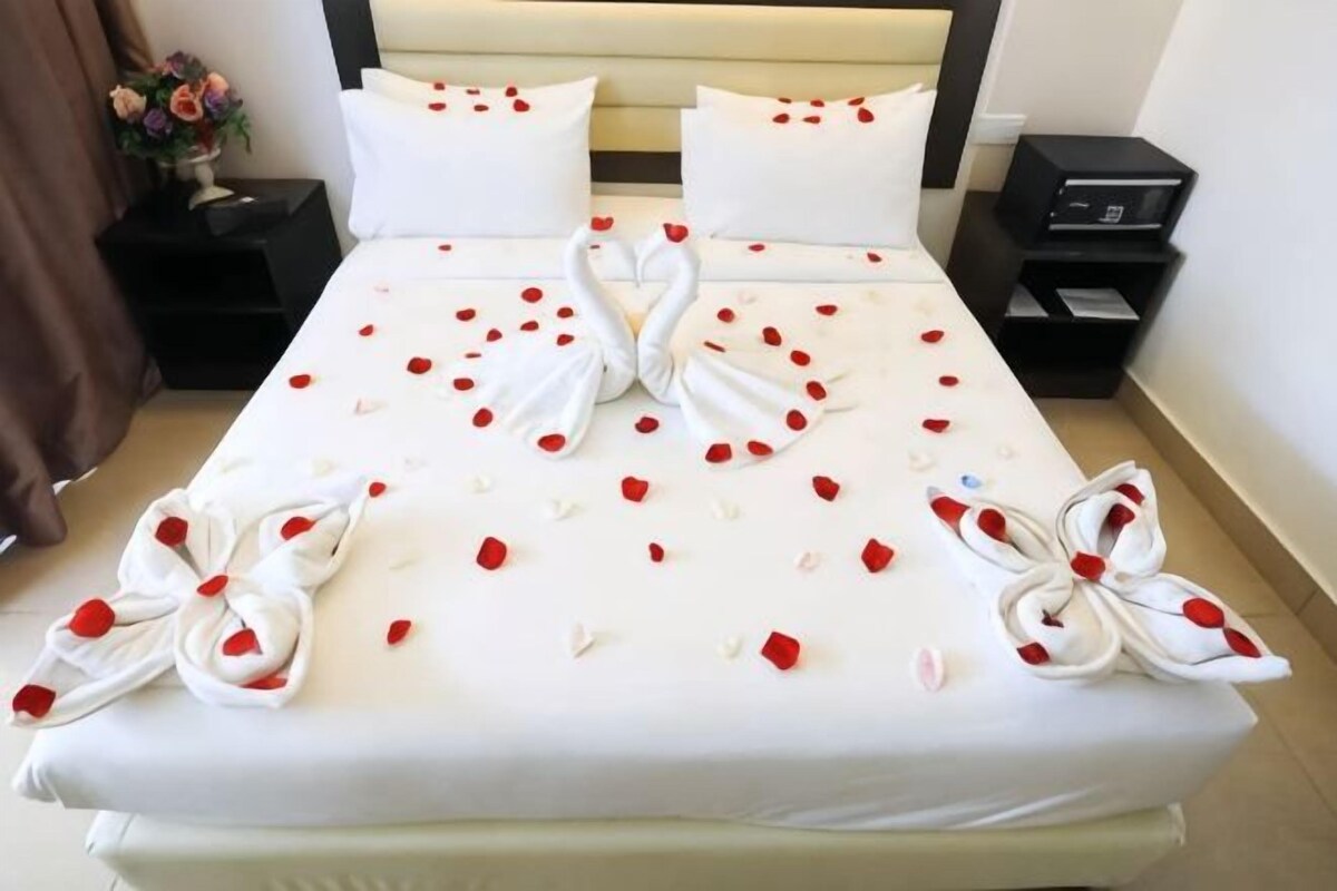 Una cama con sábanas blancas, pétalos de rosa roja y toallas blancas dispuestas en un diseño decorativo.