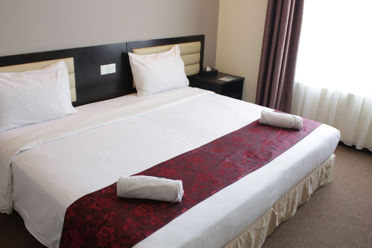 A neatly made bed with white linens and a red patterned bedspread, two white pillows, and a folded towel on the bed.