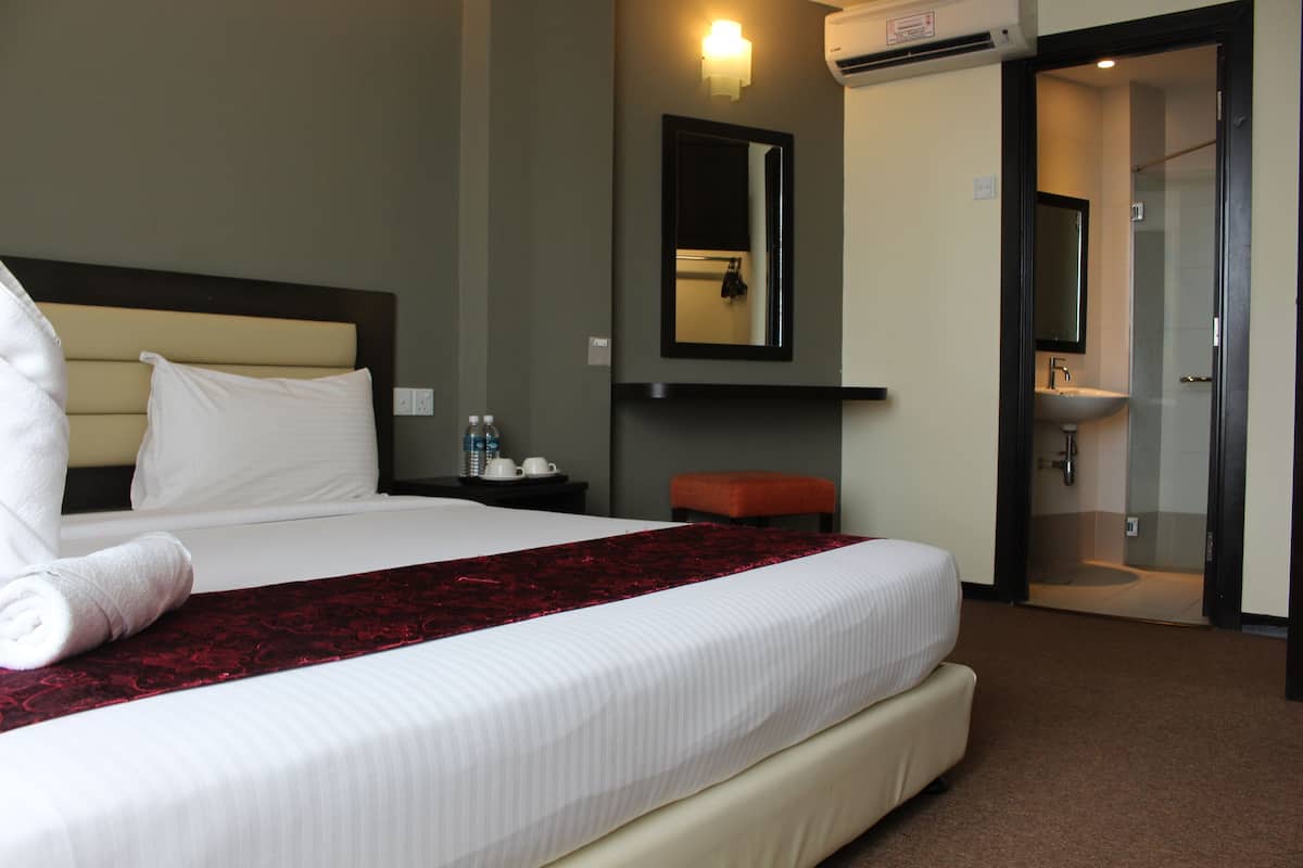 A hotel room with a large bed, a bedside table with a lamp, a mirror, and a bathroom visible through an open door.