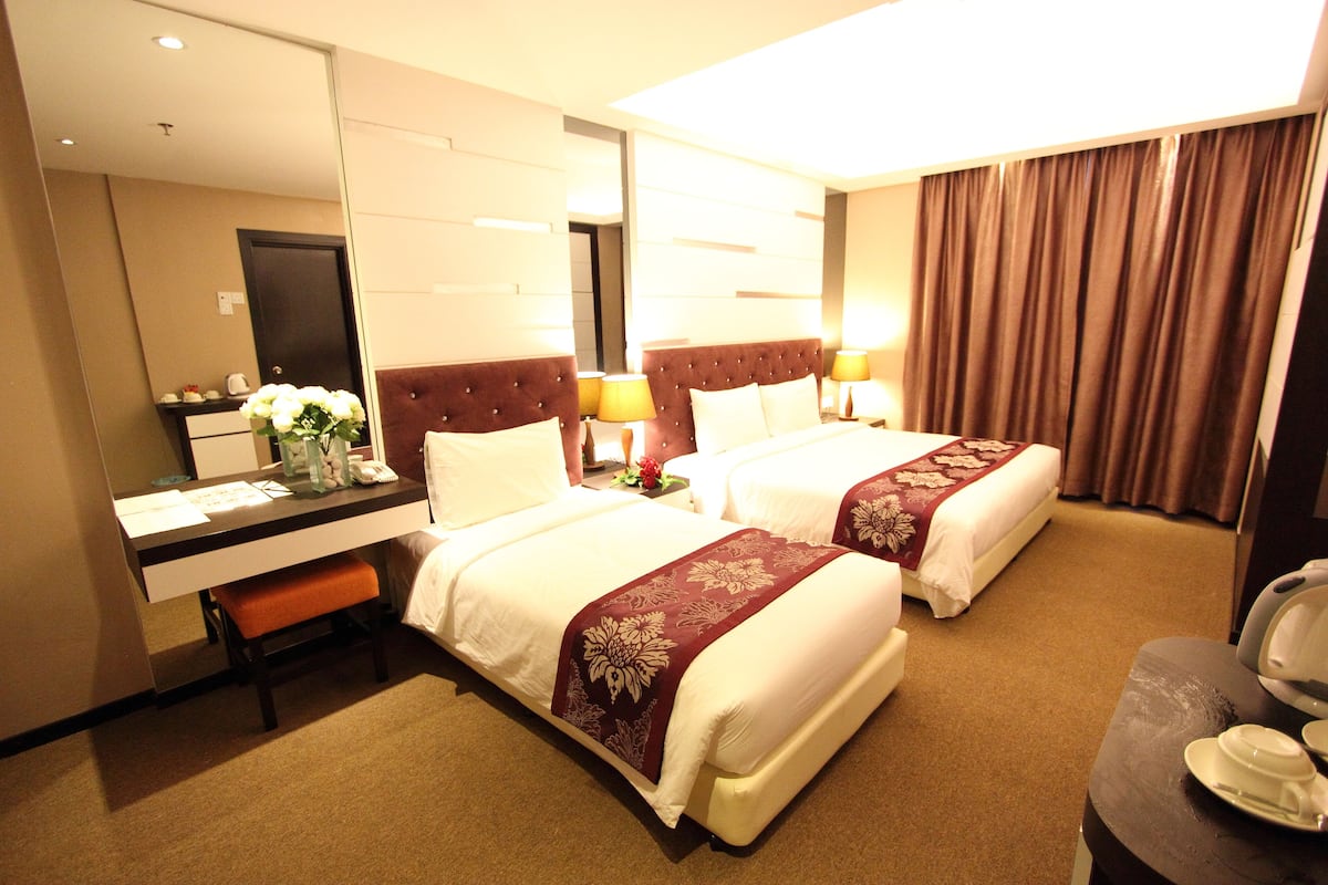 A hotel room with two beds, a desk, a mirror, and a bathroom door.