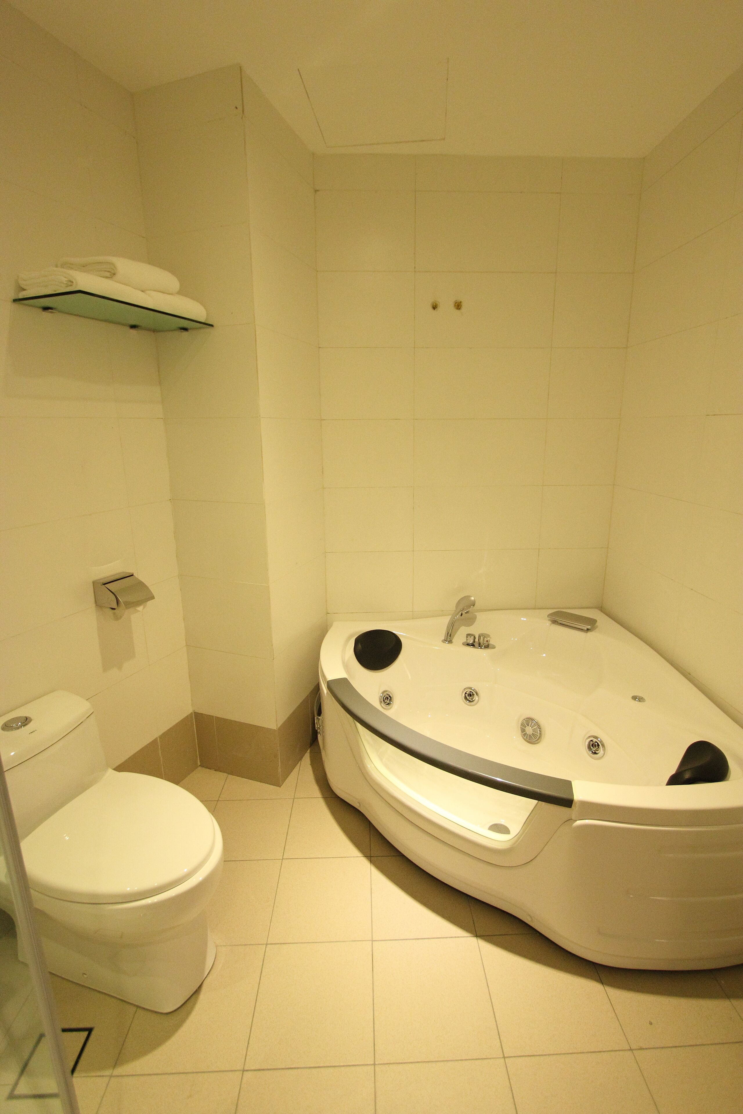 A bathroom with a white toilet, a bathtub, and a shelf above the toilet.