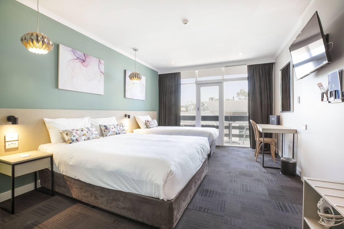 A hotel room with two beds, a desk, a TV, and a balcony with a view.