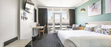 A hotel room with a bed, desk, chair, and a balcony with a view.