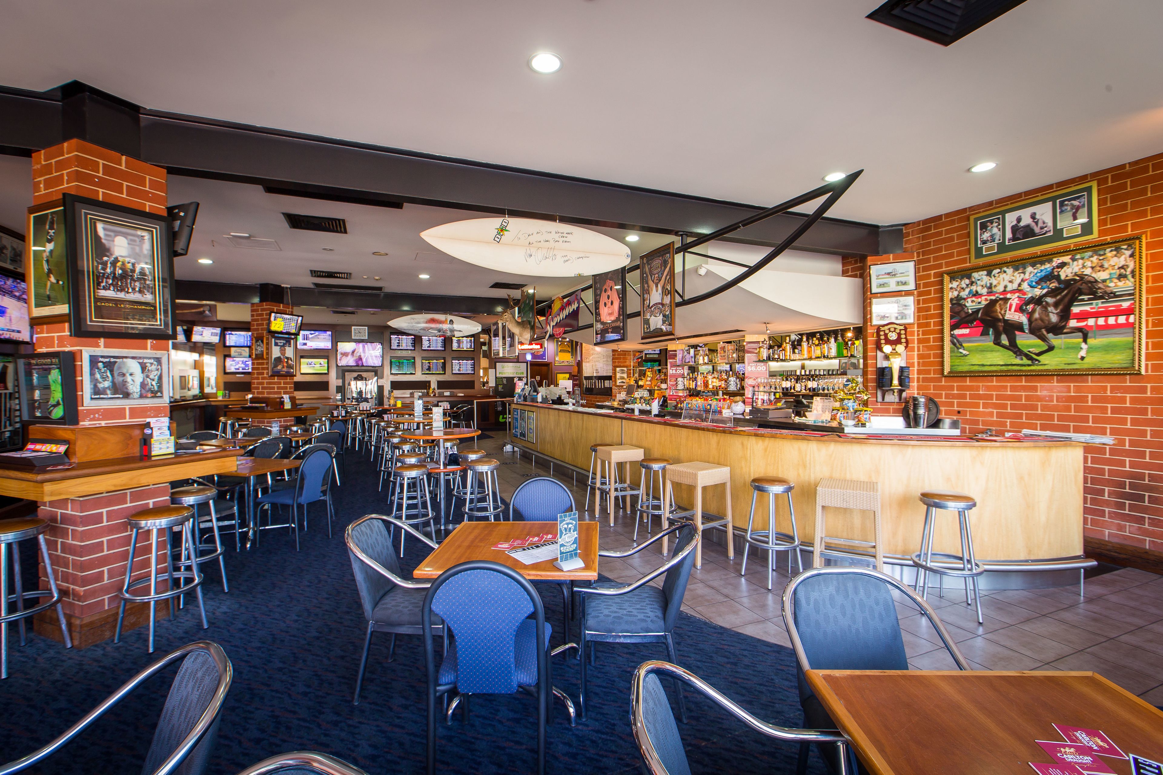 Een restaurant met meerdere tafels en stoelen, een bar en verschillende ingelijste foto’s op de muren.