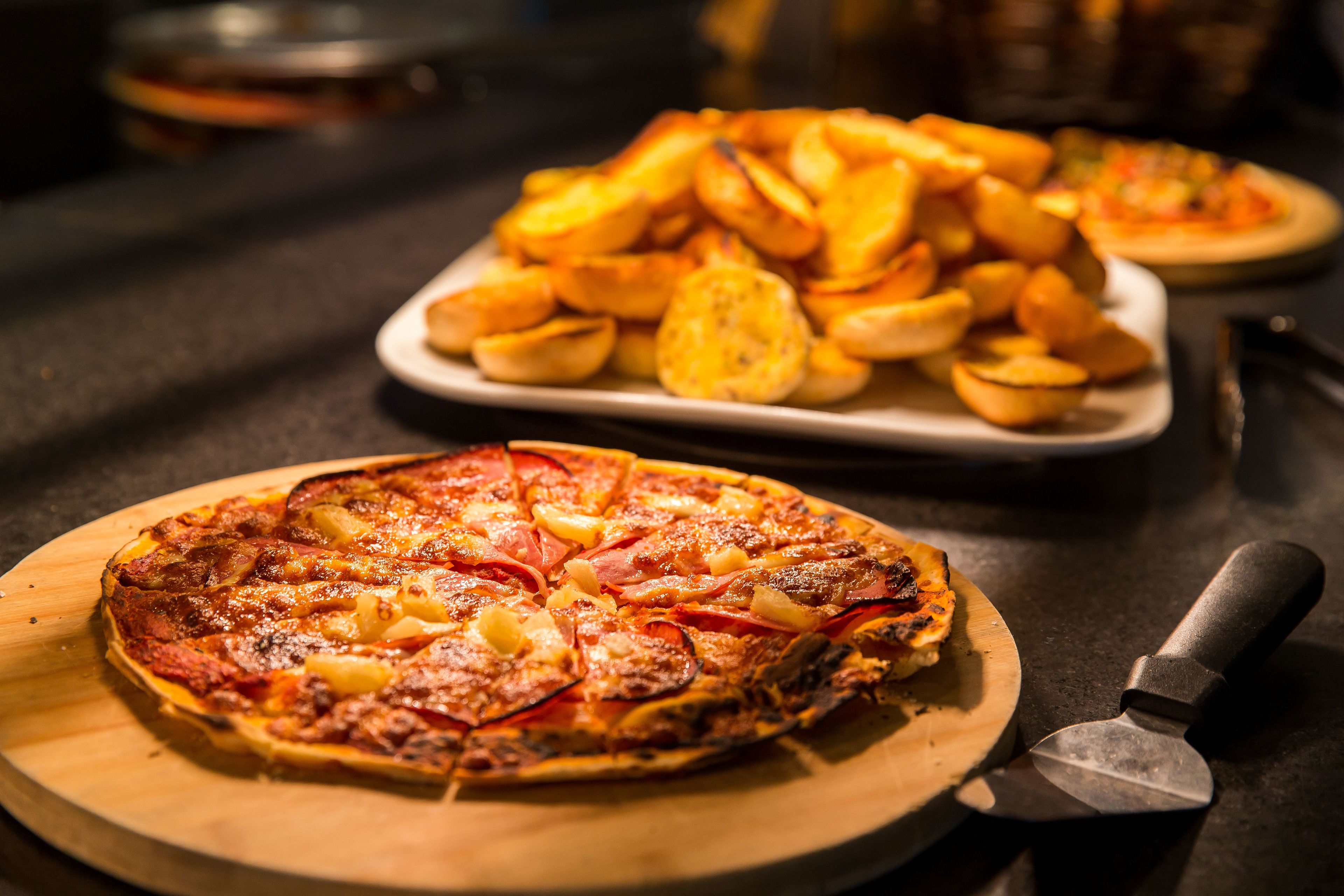Pizza op een houten plank met een pizzames er naast.
