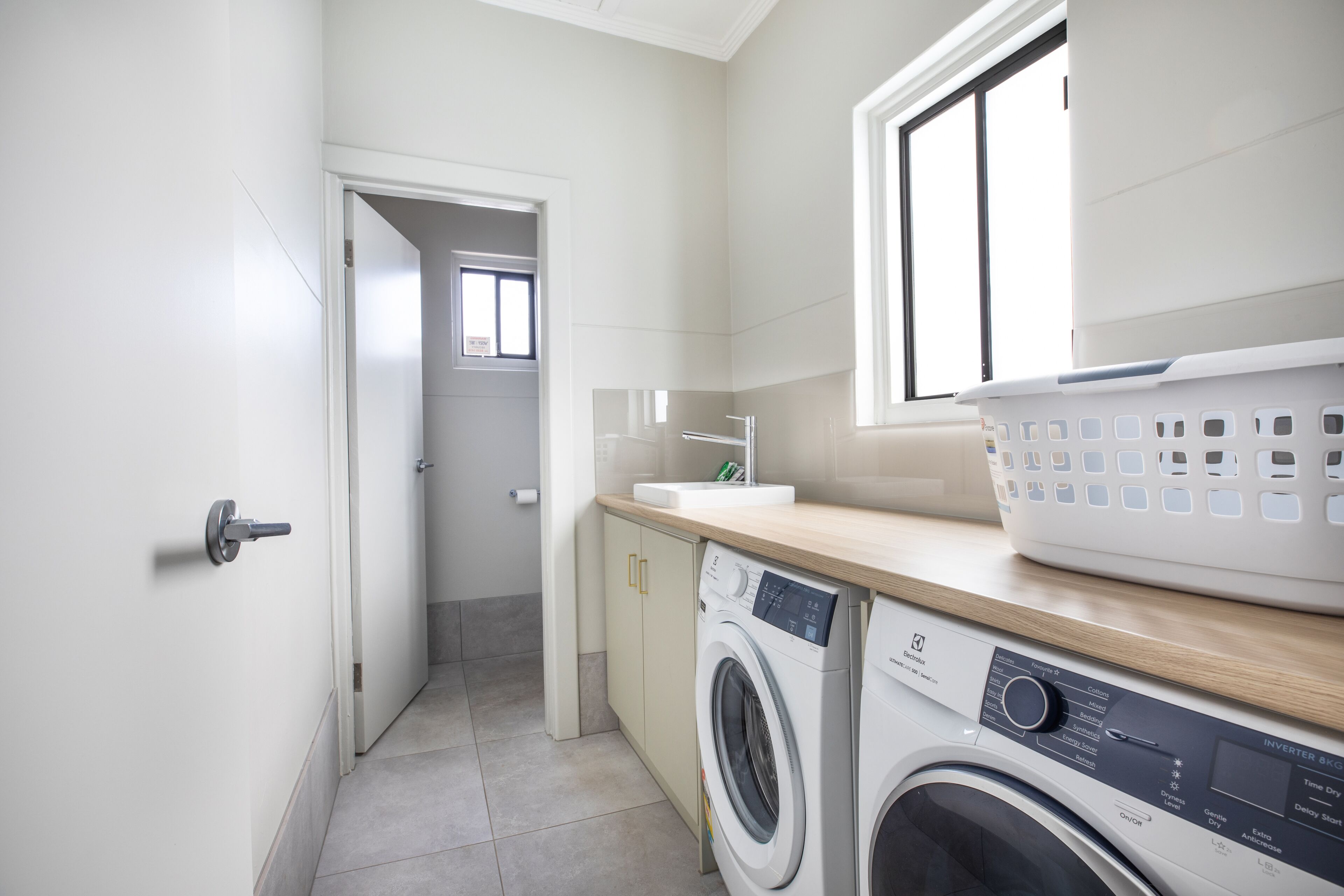 A laundry room with a washing machine, a dryer, a sink, and a window.