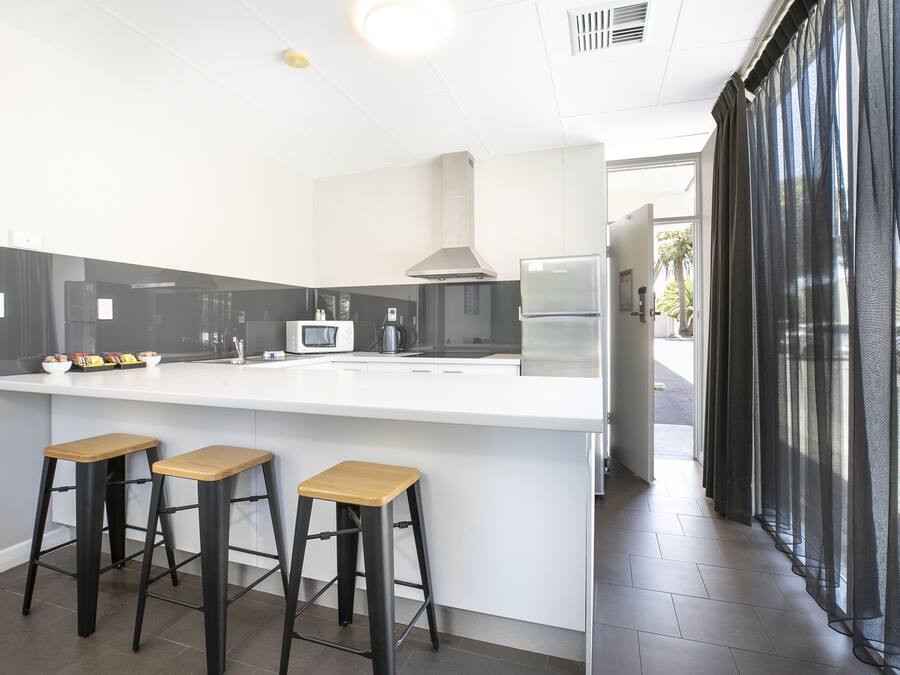 Una cocina moderna con encimera blanca, taburetes negros, una campana extractora de acero inoxidable y un refrigerador.
