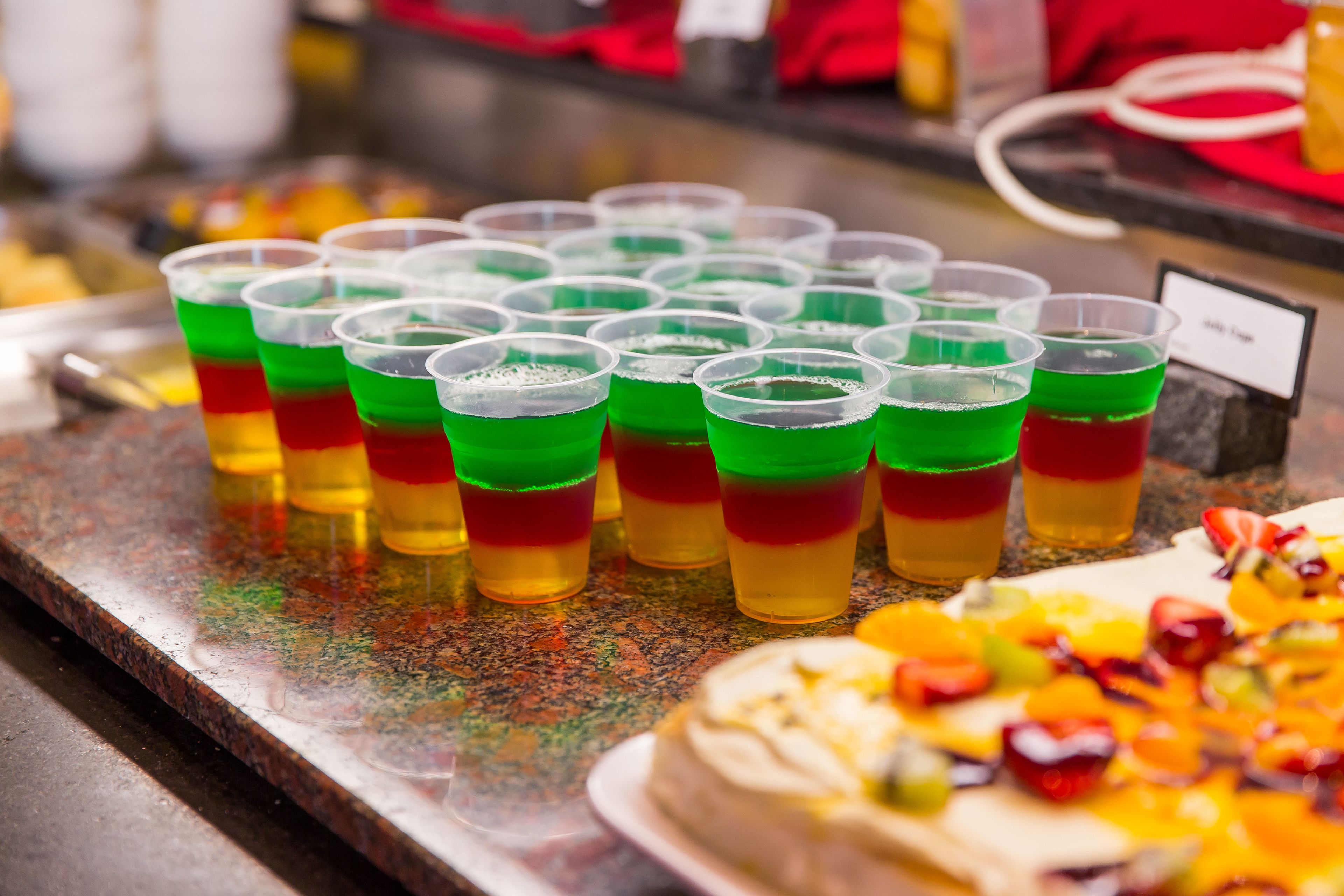 Una barra con varias tazas de bebidas en capas y un postre cubierto de fruta.