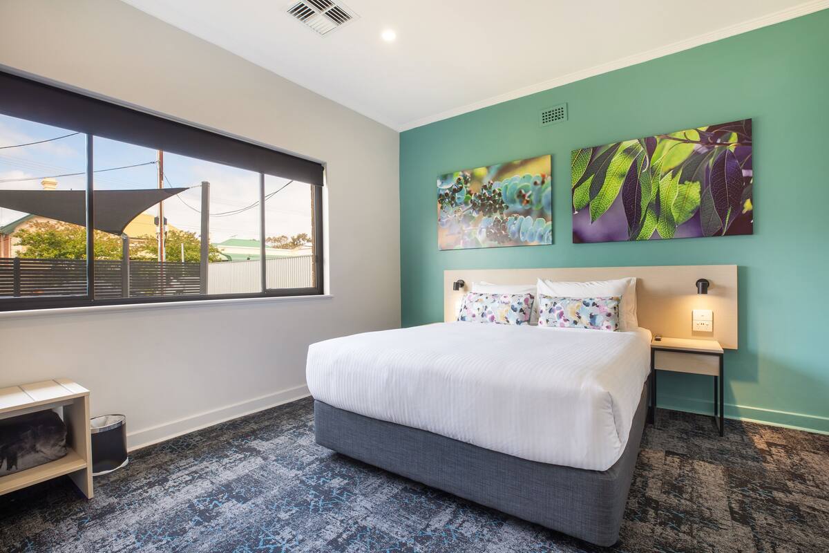 A hotel room with a large bed, a window with a view, and two wall art pieces.