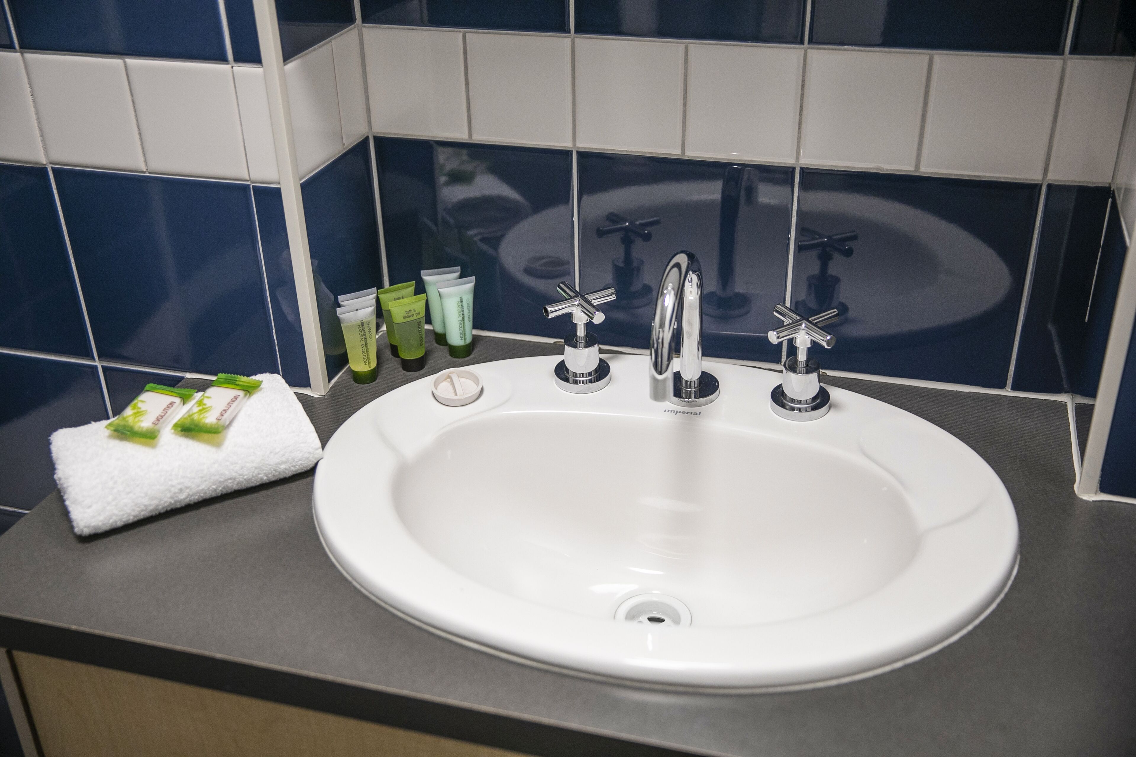 A white sink with a modern faucet, a towel, and toiletries on a countertop.