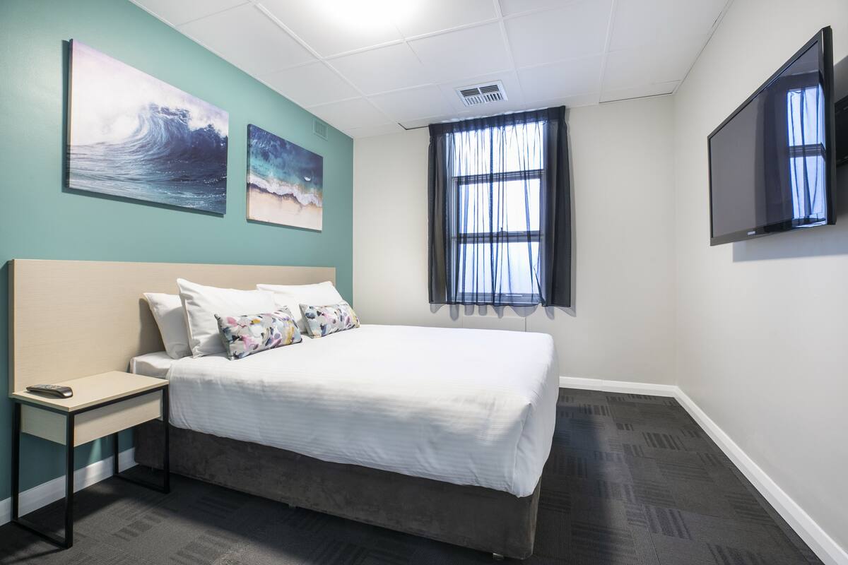 A hotel room with a bed, a desk, a TV, and artwork on the walls.