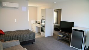 Een kleine woonruimte met een bank, een bed, een kitchenette en een televisie.