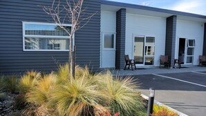 Een modern gebouw met een parkeerplaats, een terras en een aangelegde tuin met verschillende planten.