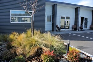 A modern building with a parking lot, outdoor seating area, and landscaped garden with various plants.