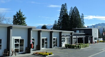 A motel with multiple rooms, a covered parking area, and a mountain view in the background.