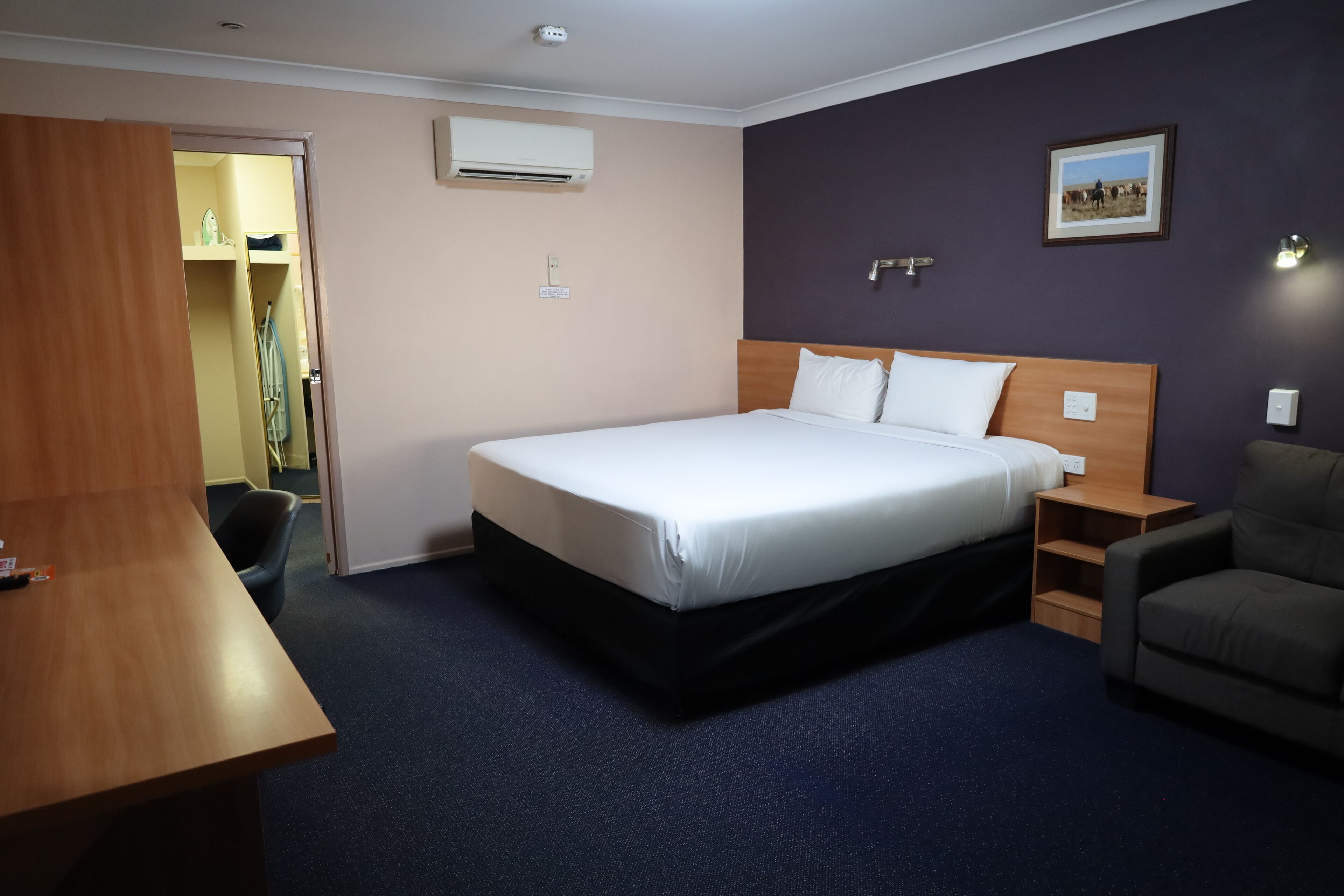 Una camera d'albergo con un letto grande, una scrivania, una sedia, un armadio e un quadro appeso al muro.