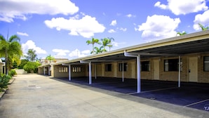 A covered parking area with multiple rooms, a clear sky, and some palm trees. - Sun Palms Motel (Allenstown)