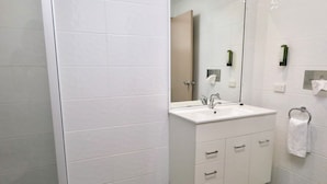 A modern bathroom with white tiles, a large mirror, a white sink, and a towel rack. - Sun Palms Motel (Allenstown)