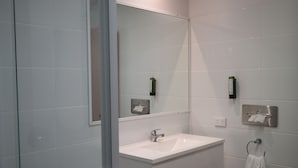 A modern bathroom with a glass shower enclosure, a white sink, and a large mirror. - Sun Palms Motel (Allenstown)