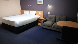 A hotel room with a bed, a sofa, a small table, and a wall-mounted air conditioner. - Sun Palms Motel (Allenstown)