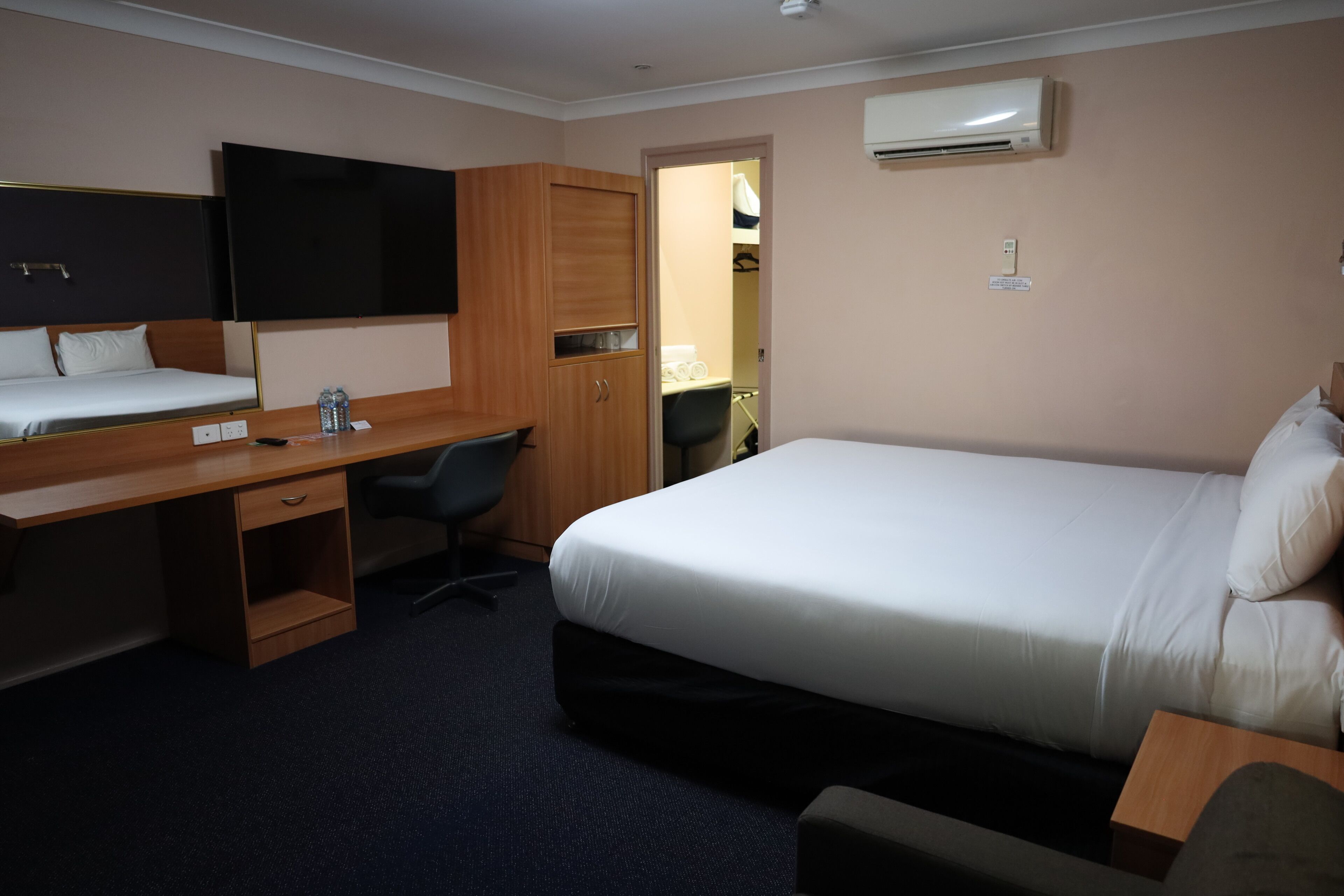 A hotel room with a bed, a desk, a chair, a wardrobe, and a television.