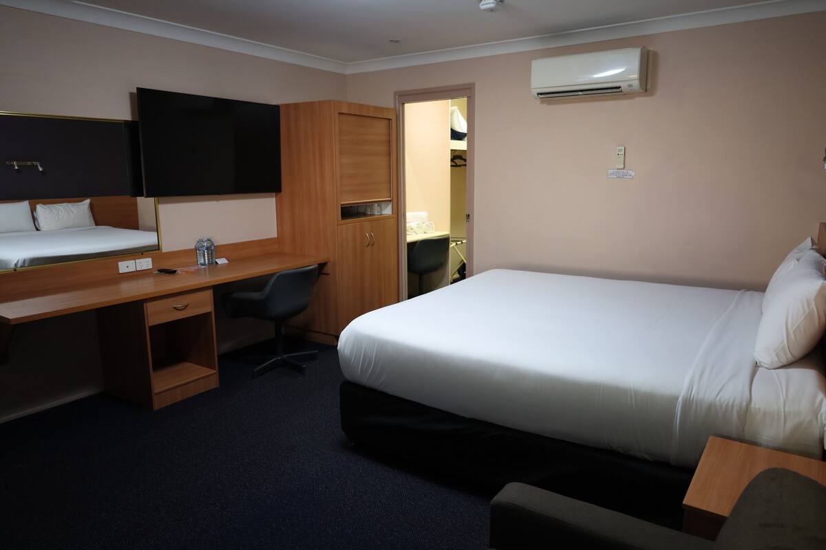 Una habitación de hotel con una cama, un escritorio, una silla, un armario y un televisor.