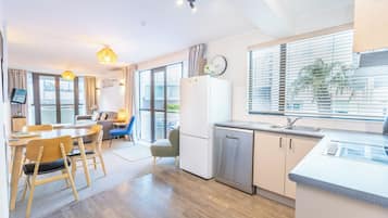 A modern kitchen with a dishwasher, a dining area with a table and chairs, and a large window with blinds.