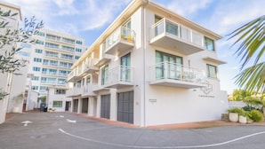 A multi-story hotel with a reception area, parking, and a clear sky. - Capri On Pilot Bay (Tauranga)