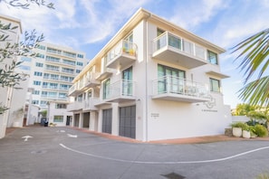 A multi-story hotel with a reception area, parking, and a clear sky. - Capri On Pilot Bay (Tauranga)