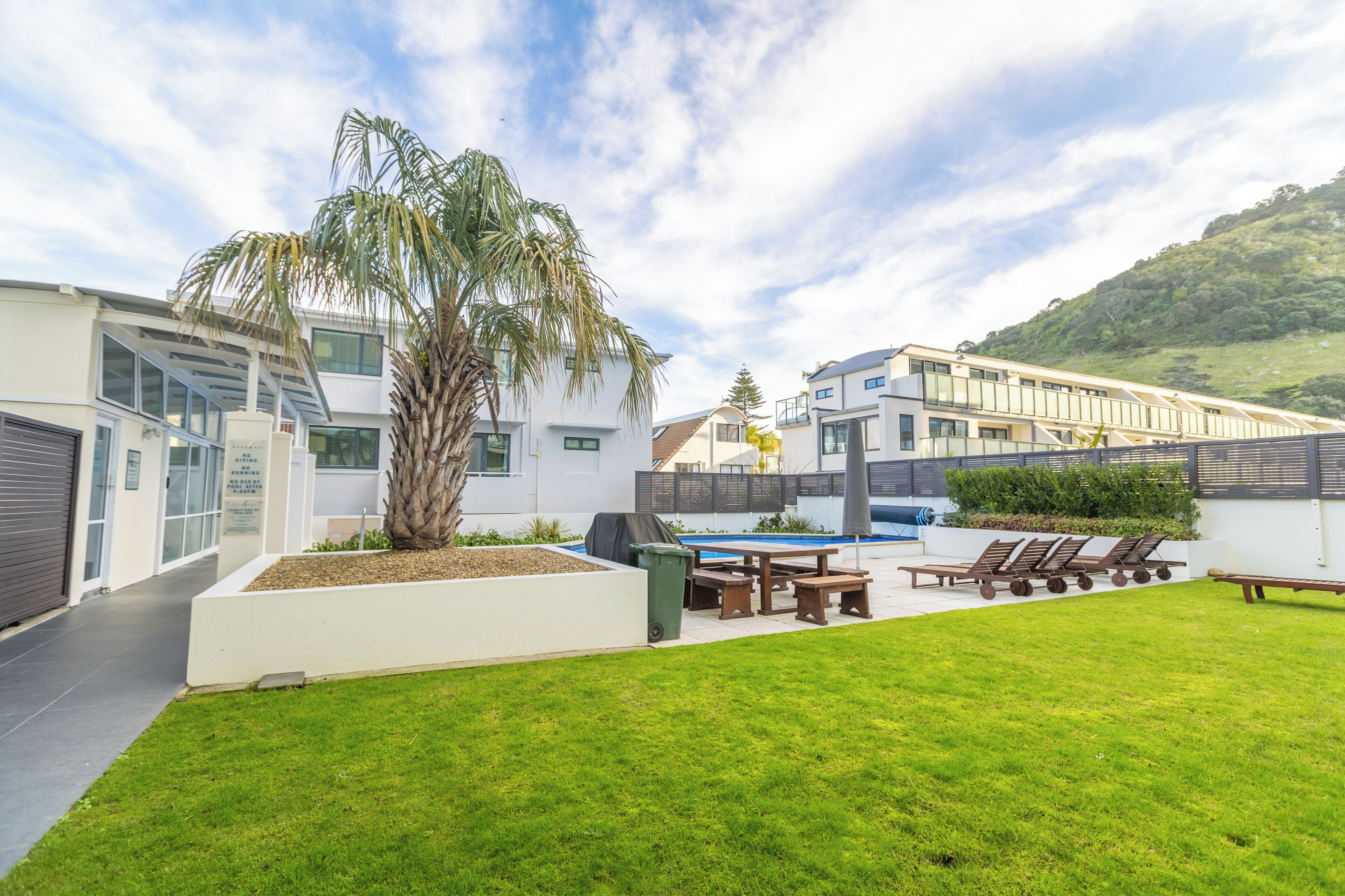 A modern residential area with a swimming pool, outdoor seating, and a well-maintained lawn.