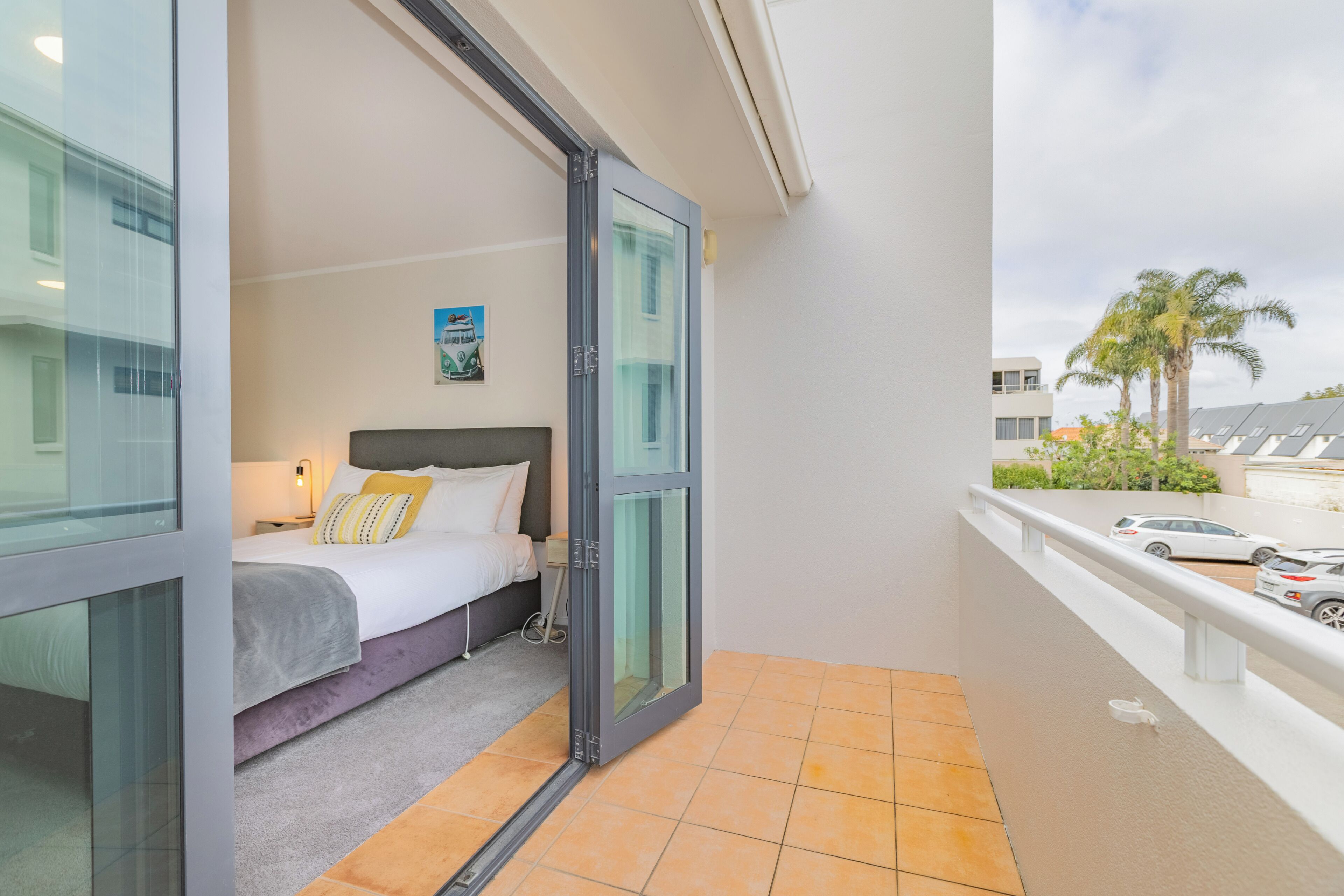 A hotel room with a bed, a nightstand, a painting, and a view of the outside.