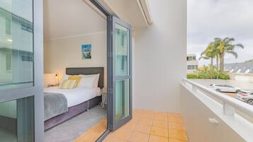 A hotel room with a bed, a nightstand, a painting, and a view of the outside.