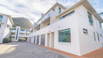 A modern multi-story residential building with a flat roof, large windows, and a paved courtyard.