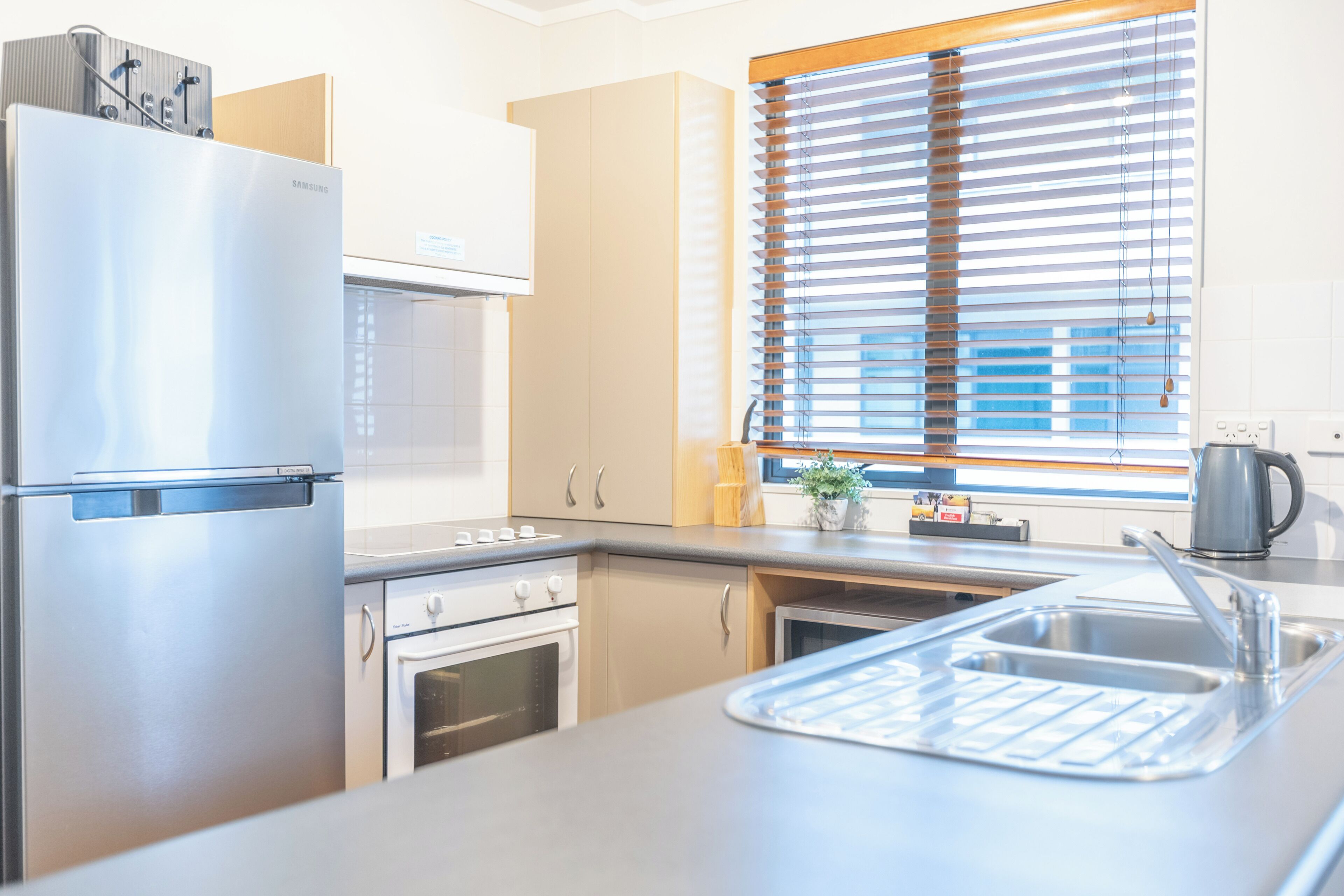 A modern kitchen with stainless steel appliances, a built-in oven, and a window with blinds.