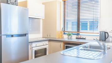 A modern kitchen with stainless steel appliances, a built-in oven, and a window with blinds.