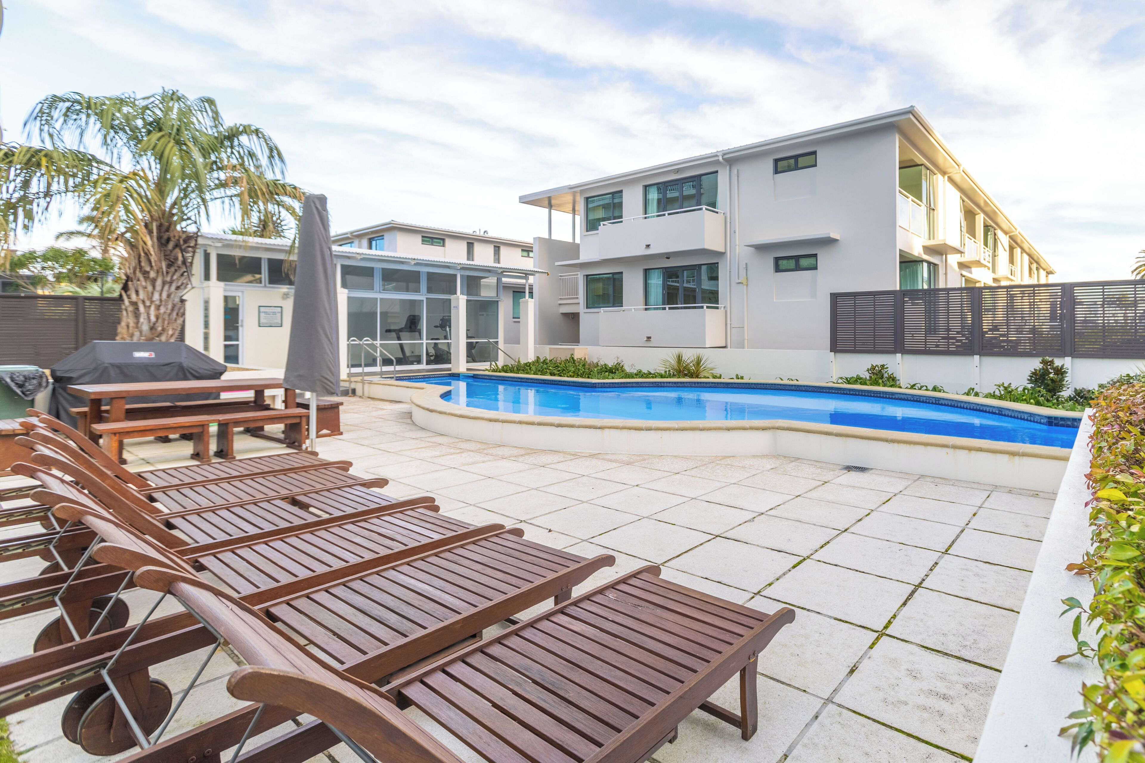 Zona junto a la piscina con sillones, una piscina y un edificio moderno con balcones.
